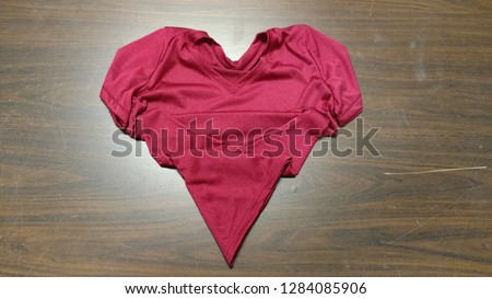 Pink t-shirt folded into a heart shape on brown wooden table