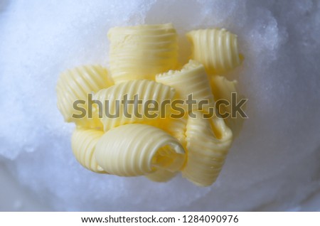 Delicious rolls of butter on a pile of fresh snow. Butter is used for cooking and baking and it adds a tasty flavor to the food. Picture is ideal for advertising dairy products,