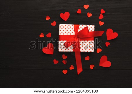 Valentine background with red handmade paper hearts and gift box on black rustic wooden planks. Happy lovers day card mockup, copy space