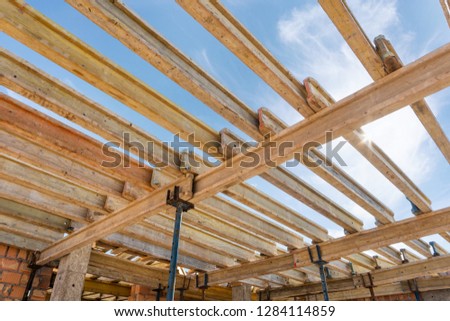 Formwork construction concept. Low angle top view photo of incomplete house with wooden ribbed plank board under roof and metal support pillars