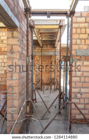 Formwork construction concept. Vertical photo of unfinished building with wooden beam under roof and metal support pipes