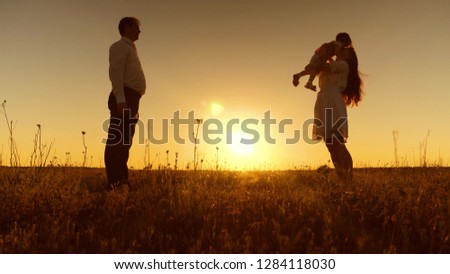 Little daughter goes to her mother in her arms at sunset. Happy mother hugs and kisses baby. Dad, mom and baby are playing for walk in evening. First steps.