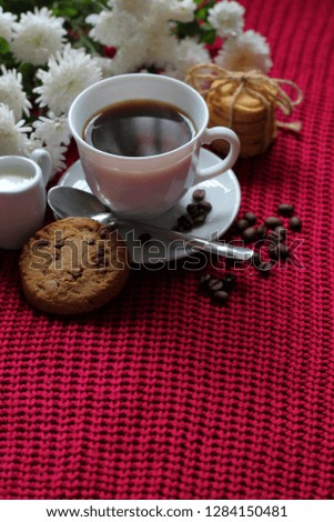 Traditional continental breakfast, cup of coffee espresso with milk, pile of delicious chip cookies tied with twine and white flowers on a red knitted background. Good morning concept. Enjoy slow life