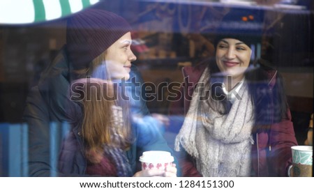 Two friends drink coffee in a cafe with a view to the street