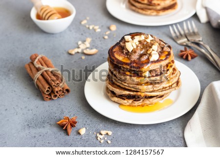 Pancakes with cashew nuts, honey, cinnamon and anise on a white plate. Perfect breakfast. Grey concrete background. Copy space.