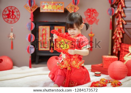 Chinese baby girl traditional dressing up hold a Fu means 'lucky' greeting sign  against  FU means lucky ornament background