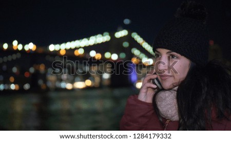 Young woman takes a phone call at Brooklyn Bridge by night