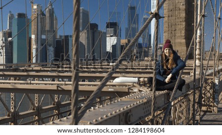 Young and reckless girl sits on the rim of Brooklyn Bridge New York