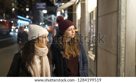 Two girls on a shopping trip in New York walk along shop windows
