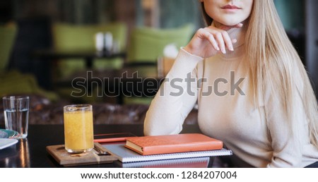 Blonde girl sitting in the restaurant with orange drink on the table.