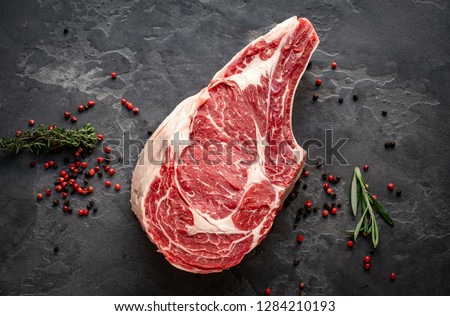 raw cowboy steak with seasonings on stone background, prime rib eye on bone, top view