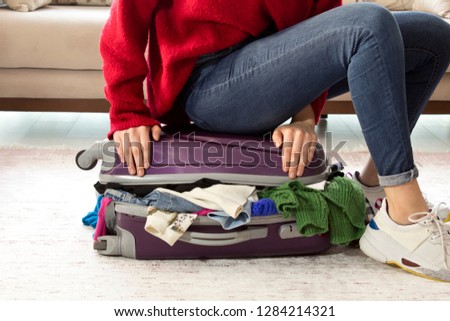 A picture of a woman having problem with packing a suitcase