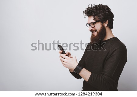 Handsome bearded model is posing with phone in hands over white background Royalty-Free Stock Photo #1284219304