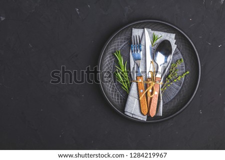 Rustic vintage set of cutlery knife, fork and spoon in black ceramic plate. Black stone concrete surface background. Top view, copy space.