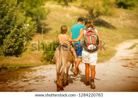Summer, sunny day. Mom rolls the baby on a donkey on the road among the mountains of Crimea. Picture taken in Ukraine. Kiev region. Horizontal frame. Color image toning
