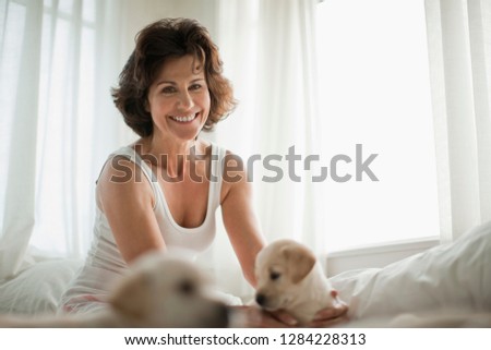 Smiling mid adult woman sitting on the bed with Labrador puppies.