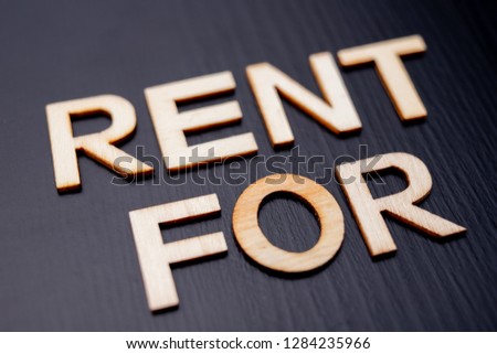 The inscription is arranged from letters cut out of wood on the table. The word – rent for. Dark background.