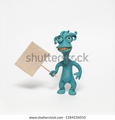 Funny blue monster alien with a sign in his hand. Plasticine character on a white background
