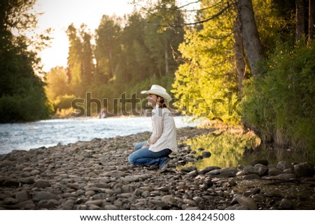 Smiling young woman crouching on a riverbank.