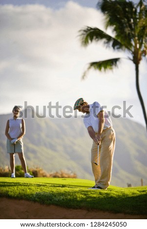 Man plays golf as a female golfer looks on.