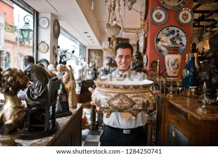 Portrait of a smiling mid-adult businessman holding an antique bowl while standing inside an antique store.