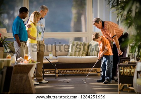 Young boy getting golf tips from his mid-adult father as his mother and two men watch.