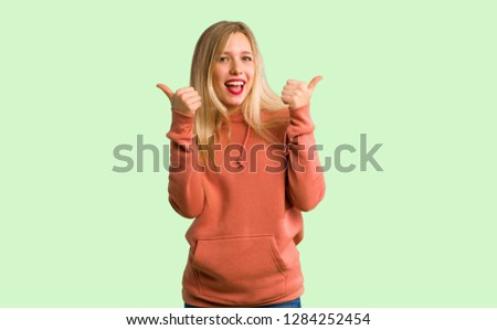 Young girl giving a thumbs up gesture with both hands and smiling on green background