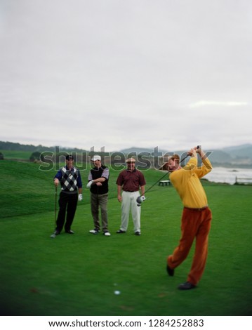 Man taking a swing with a golf club while playing golf with his friends on a golf course.