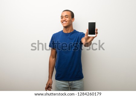 Young african american man on white wall showing the mobile