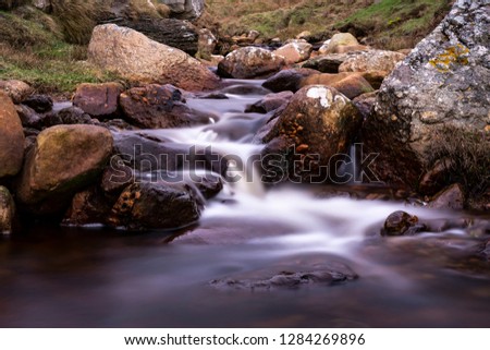 A photo of a long exposed creek flowing through a stream with beautiful rocks and stones guiding its way with breathtaking greenery from The Emerald Isle's.