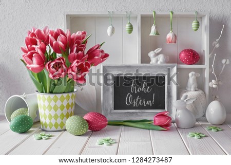 Springtime background with Easter decorations and a chalk board. Display cabinet with different objects and pink tulips. Text "Frohe Ostern" on the blackboard means "Happy Easter" in German