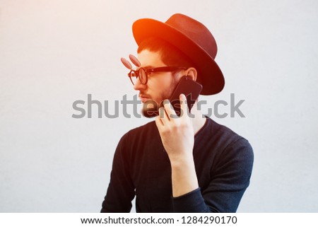Young hipster bearded guy using smartphone over white background. Wearing sunglasses and black hat.