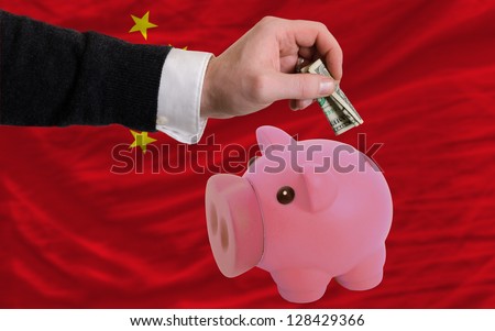 Man putting dollar into piggy rich bank national flag of china in foreign currency because of inflation