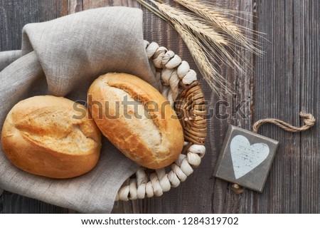 Bread buns in basket on rustic wood with wheat ears and wooden heart tag, top view