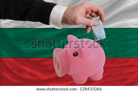 Man putting euro into piggy rich bank and national flag of bulgaria in foreign currency because of insecurity and inflation