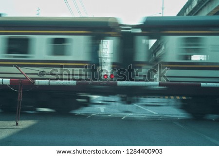 Blurred motion picture of train moving across the road with barrier and lighting sign in foreground