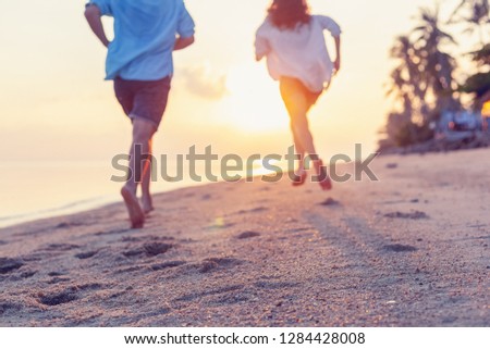 Young couple running along the sandy seashore in the rays of sunset, blurred image perfect background for travel agencies, honeymoon vacation travel in the tropics. Valentines day
