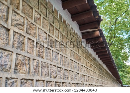 Wall of Deoksu palace in Korea with tiled stones and many brown wooden frames supporting the traditional kiwa.                               