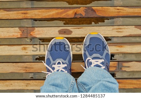 Top view of fashion navy blue sneakers with blue jeans stands on dark brown wooden walkway over water. Close up of comfortable sport shoes walking step on beautiful wood board texture pattern floor