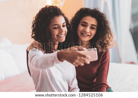 Making selfie. Two good-looking best friends smiling while taking memorable selfie sitting in the living room