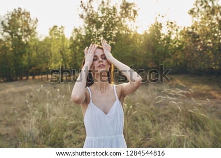  Woman in a white dress resting on the nature of the hands on the face                              
