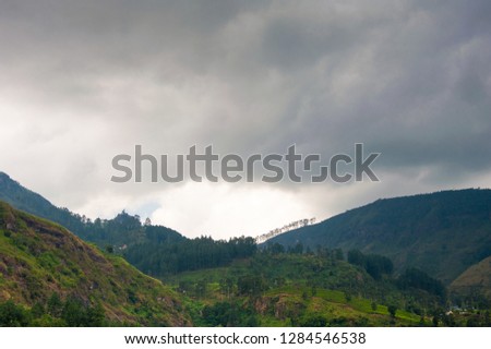 Black storm clouds hang over the highlands in tea country, Ramboda, Sri Lanka. Grey skies, green forested slopes in a scenic landscape.