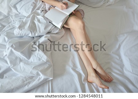 Close up lifestyle soft image of pretty young woman sitting on her cozy bed and making notes to her diary. Fall season mood. Bright colors.