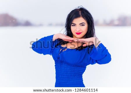 Arabic woman in bright blue chiffon long dress at snowy field. Evening fashionable dress, winter fairytale