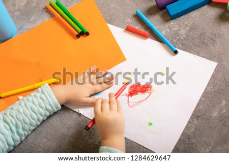 Little Child enthusiastically Draws with Pencils and felt-tip pens on colored paper and makes crafts with his hands. Kid Plays in the kids club for development and creativity. Playroom for children   