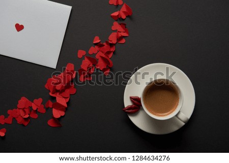 top view of white greeting card with red paper cut hearts and cup of coffee 