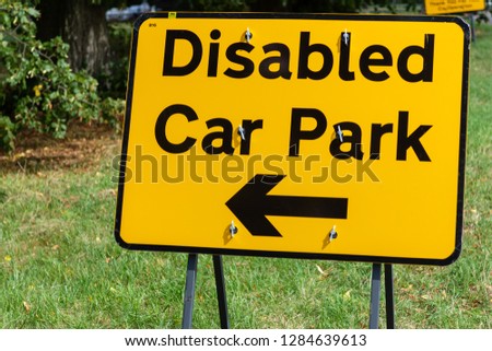 Yellow traffic sign indicates to drivers which way to the disabled car park
