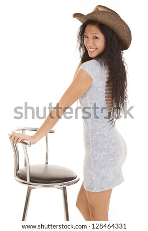 A woman in her cowgirl hat standing by her stool with a smile on her face.