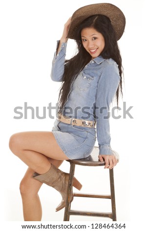 A woman sitting on her stool with a smile on her face and her hand on her cowgirl hat.