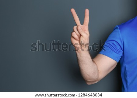 Young man showing victory gesture on color background. Space for text